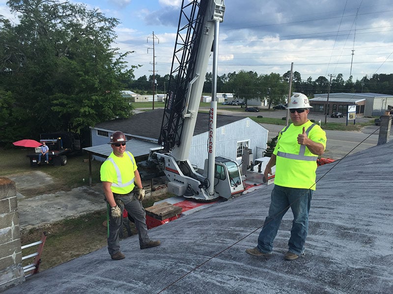 Professional arborists assess roofline clearance during storm damage evaluation at commercial property in Aiken area.