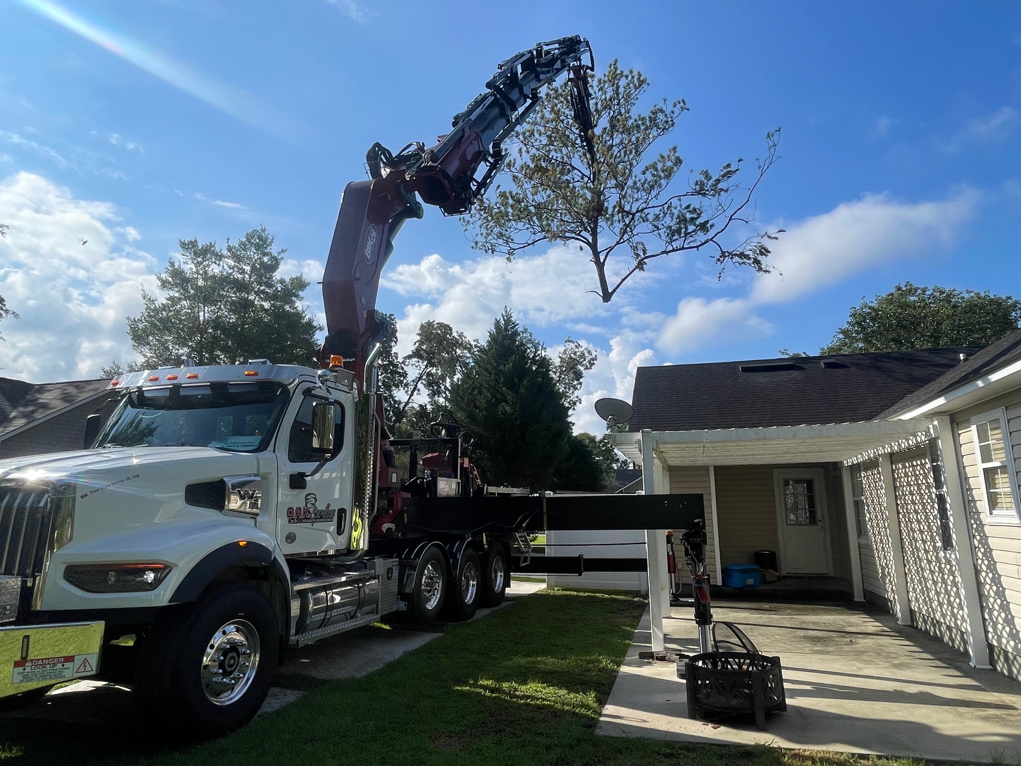 Hydraulic crane truck with grapple attachment lifting a large tree during professional removal service in residential Aiken area.